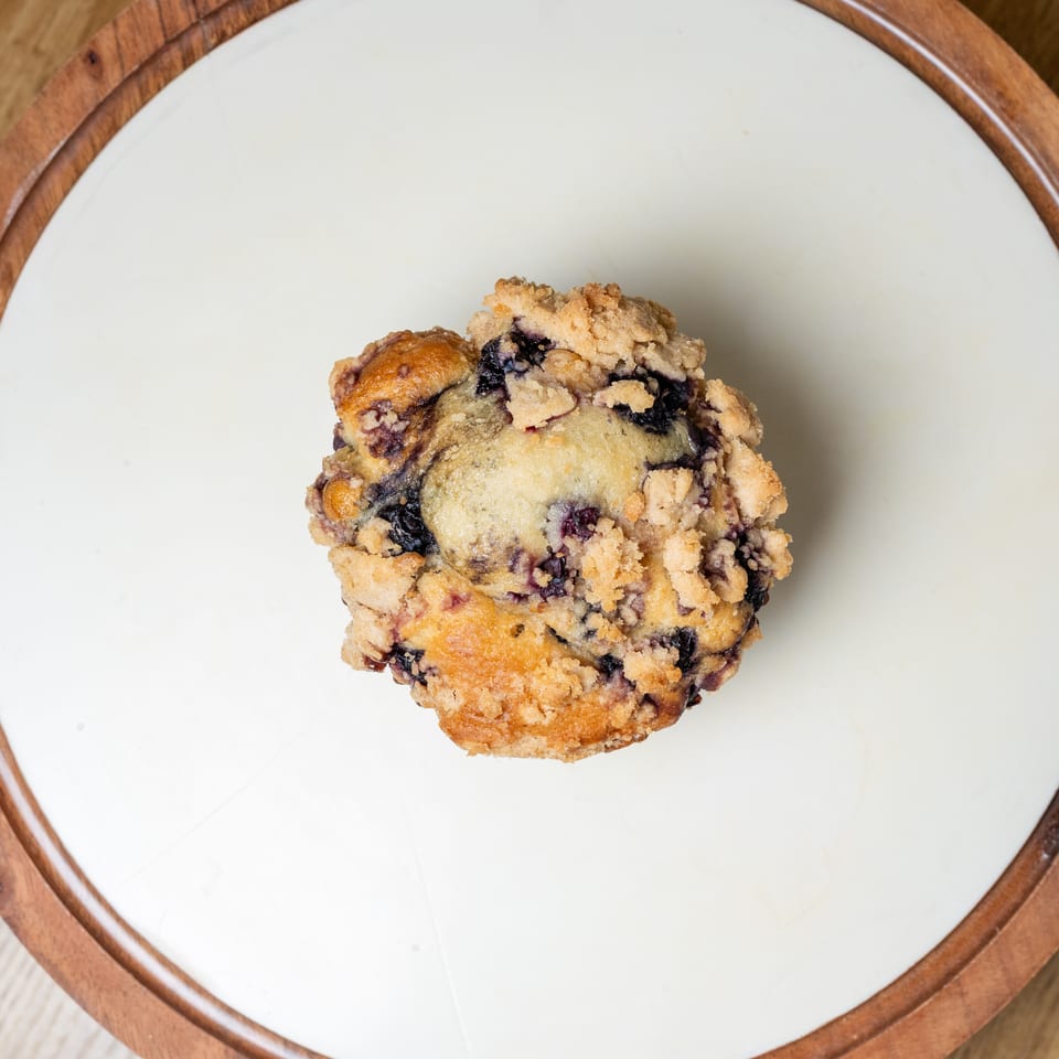 Blueberry muffin with a crumb topping centered on a white plate with a wooden rim.