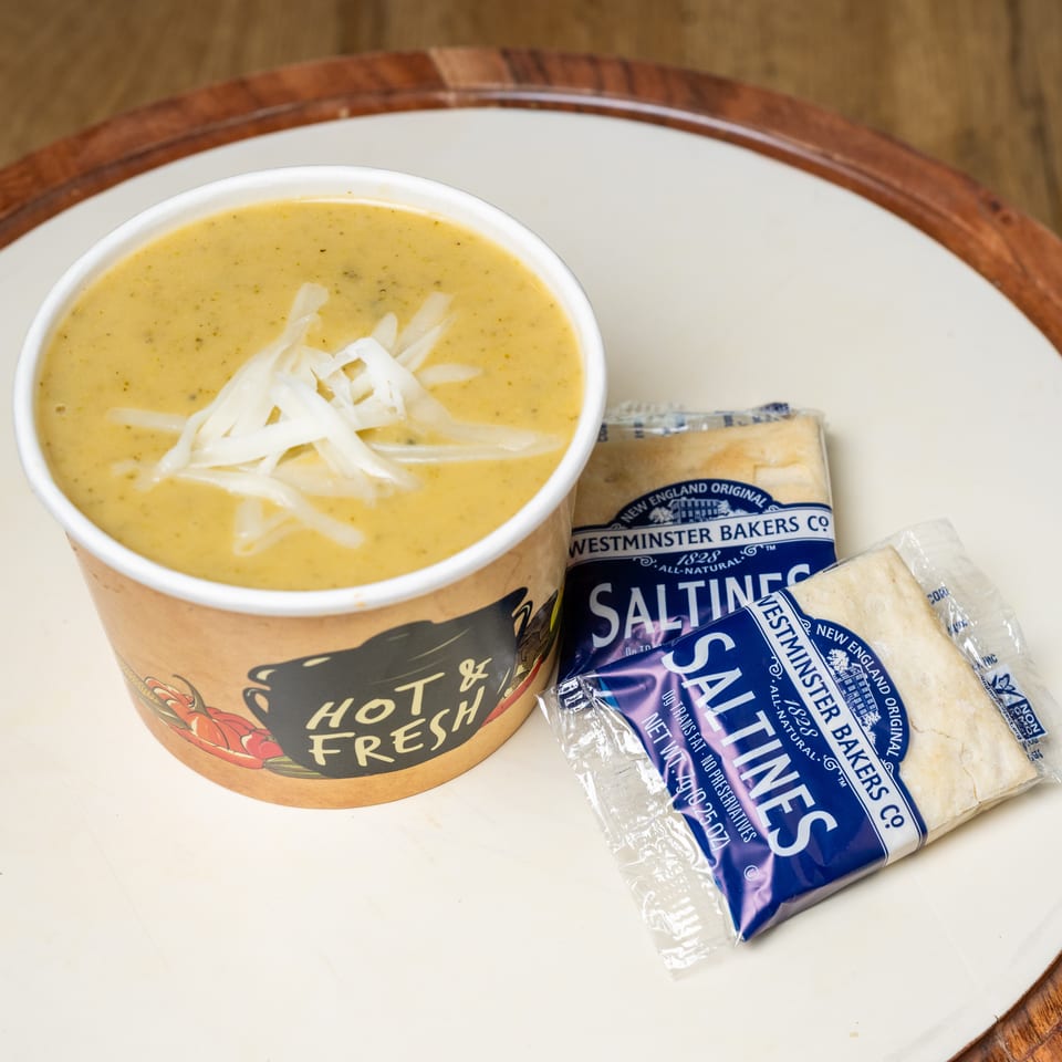 Bowl of creamy soup topped with shredded cheese, served with packaged Westminster Bakers saltine crackers on a wooden table.