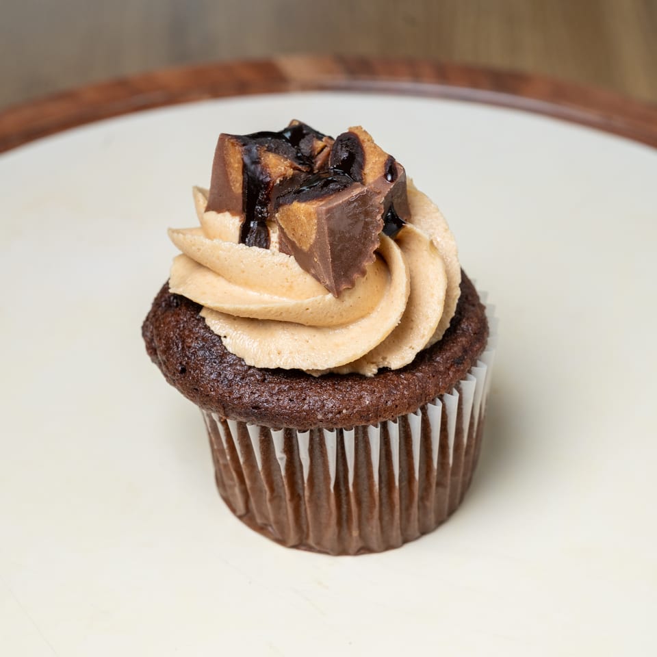 Chocolate cupcake topped with swirled peanut butter frosting, chocolate drizzle, and chunks of peanut butter cups.