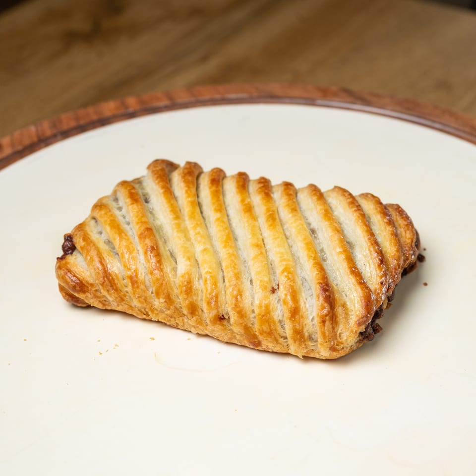 Golden-brown lattice-topped puff pastry rests on a white plate atop a wooden table.