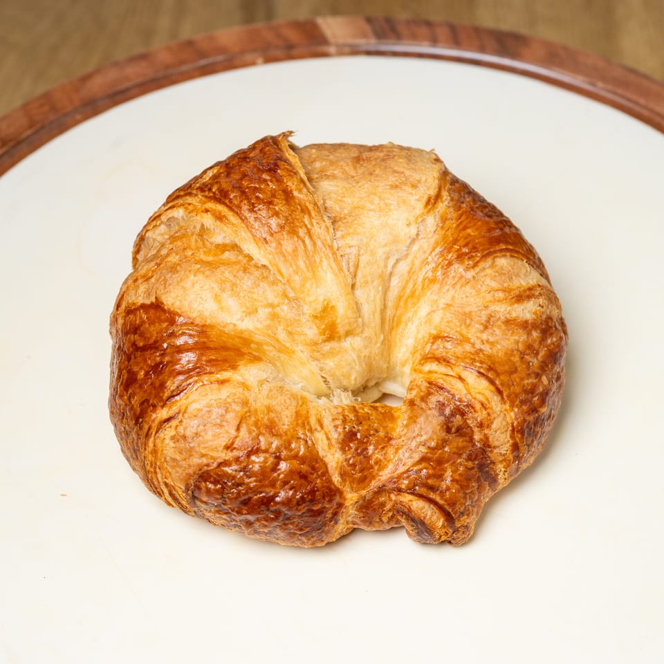 Golden-brown, flaky croissant-shaped pastry served on a white plate with a wooden rim.