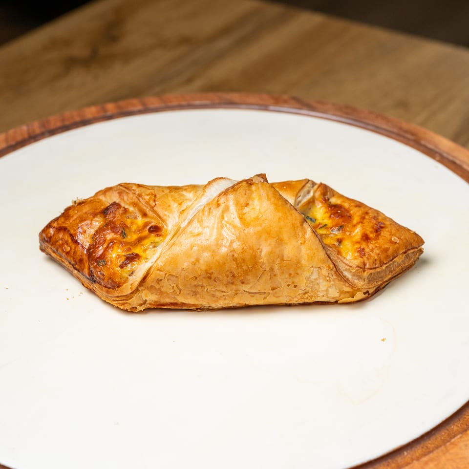 Golden-brown flaky pastries filled with melted cheese, arranged on a white plate atop a wooden table.