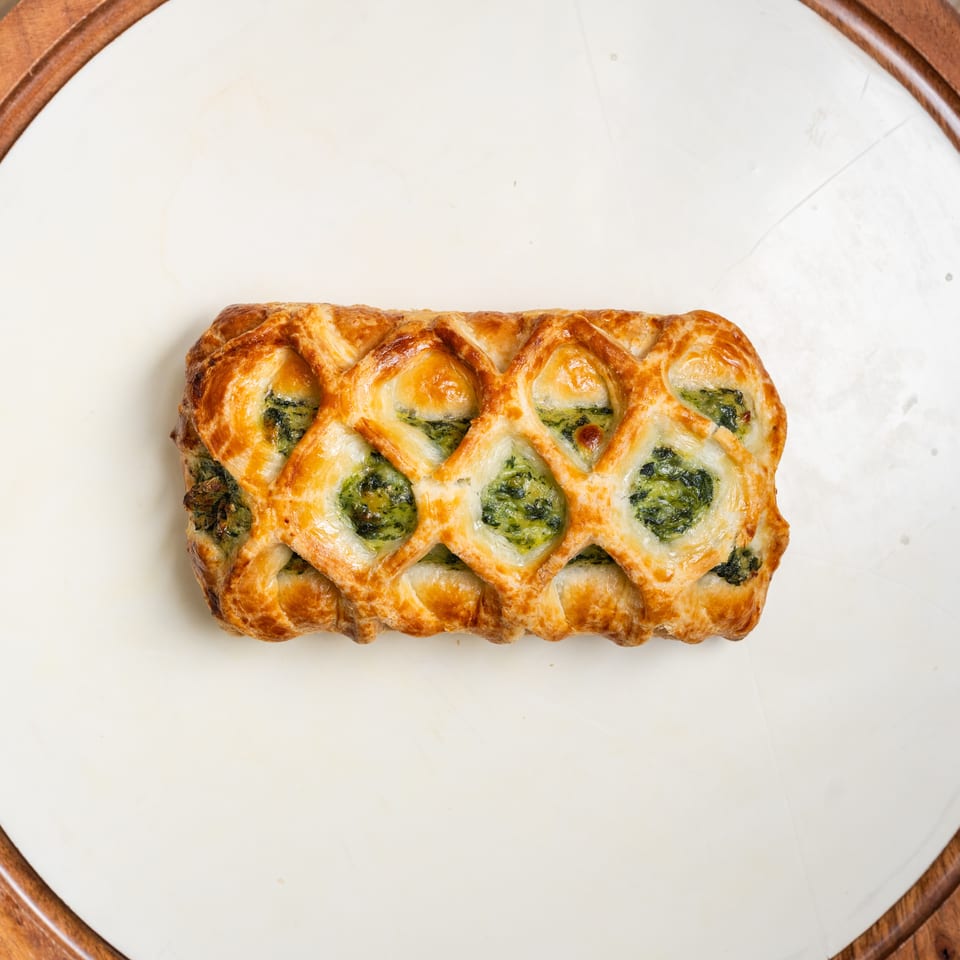 Golden lattice pastry filled with green spinach mixture, centered on a white plate with a wooden rim.